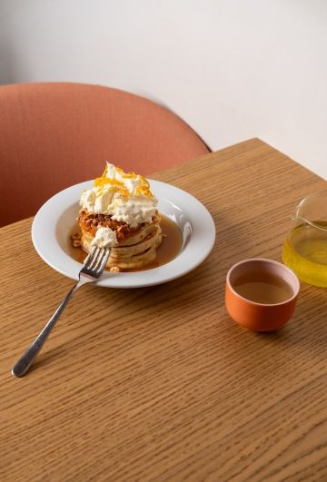 Palacinky s šlehačkou a pomerančovou kůrou na talíři vedle oranžového hrnku na dřevěném stole.
