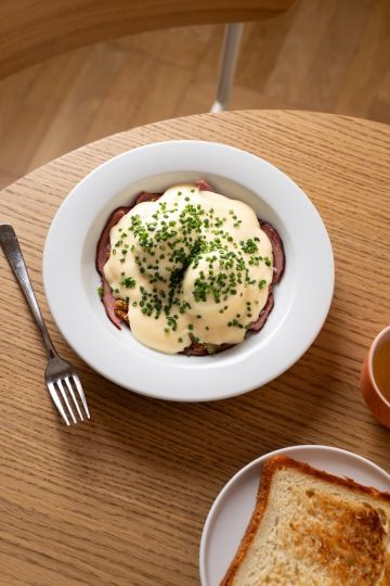 Vejce Benedikt pokrytá omáčkou a pažitkou na talíři vedle toastu na dřevěném stole.